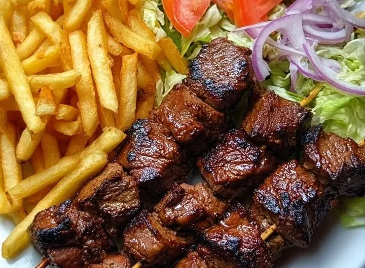 Crispy grilled beef skewers with fries and garden salad on a serving plate