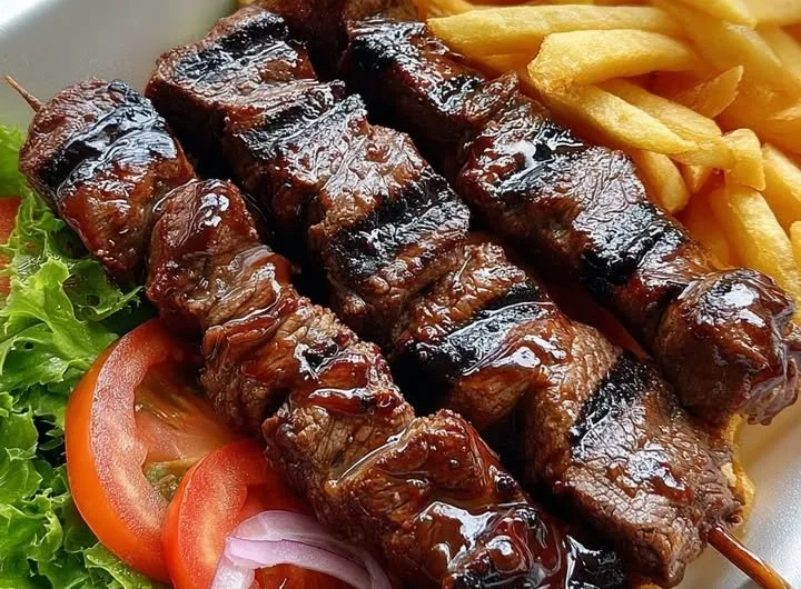 Grilled beef skewers served with crispy fries on a barbecue platter.