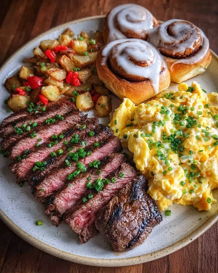 Steak Breakfast Plate with scrambled eggs and cinnamon rolls served on a white plate.